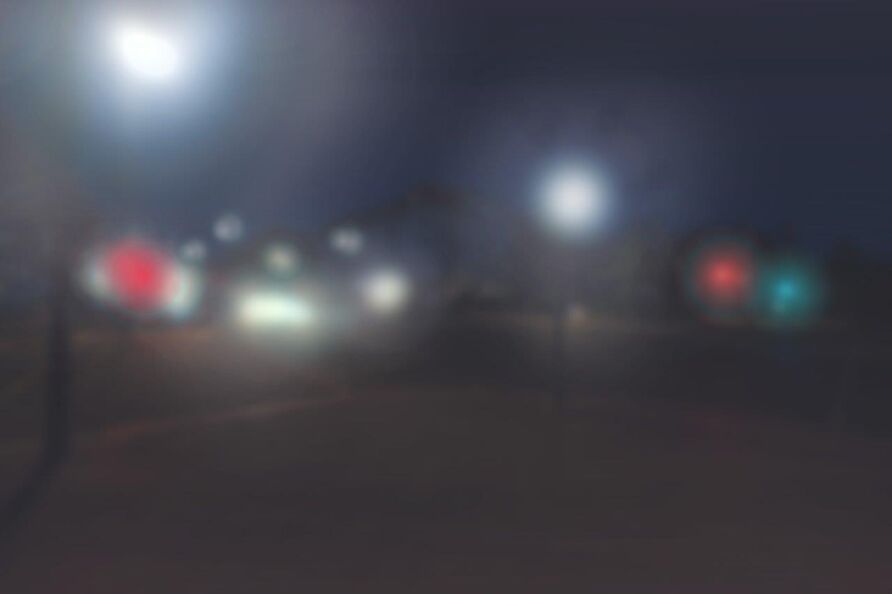 Foto: Blick auf eine Straße. Dunkle, nicht erkennbare Formen mit hellen, verschiedenfarbigen und teils runden Lichtflecken.