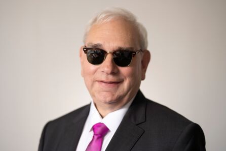 Foto: Portrait von Hans-Werner Lange. Er ist Mitte 60, hat kurze, weiße Haare und ein volles Gesicht. Er trägt ein weißes Hemd, darüber ein dunkles Jackett, dazu eine purpurfarbene Krawatte und eine dunkel getönte Brille.